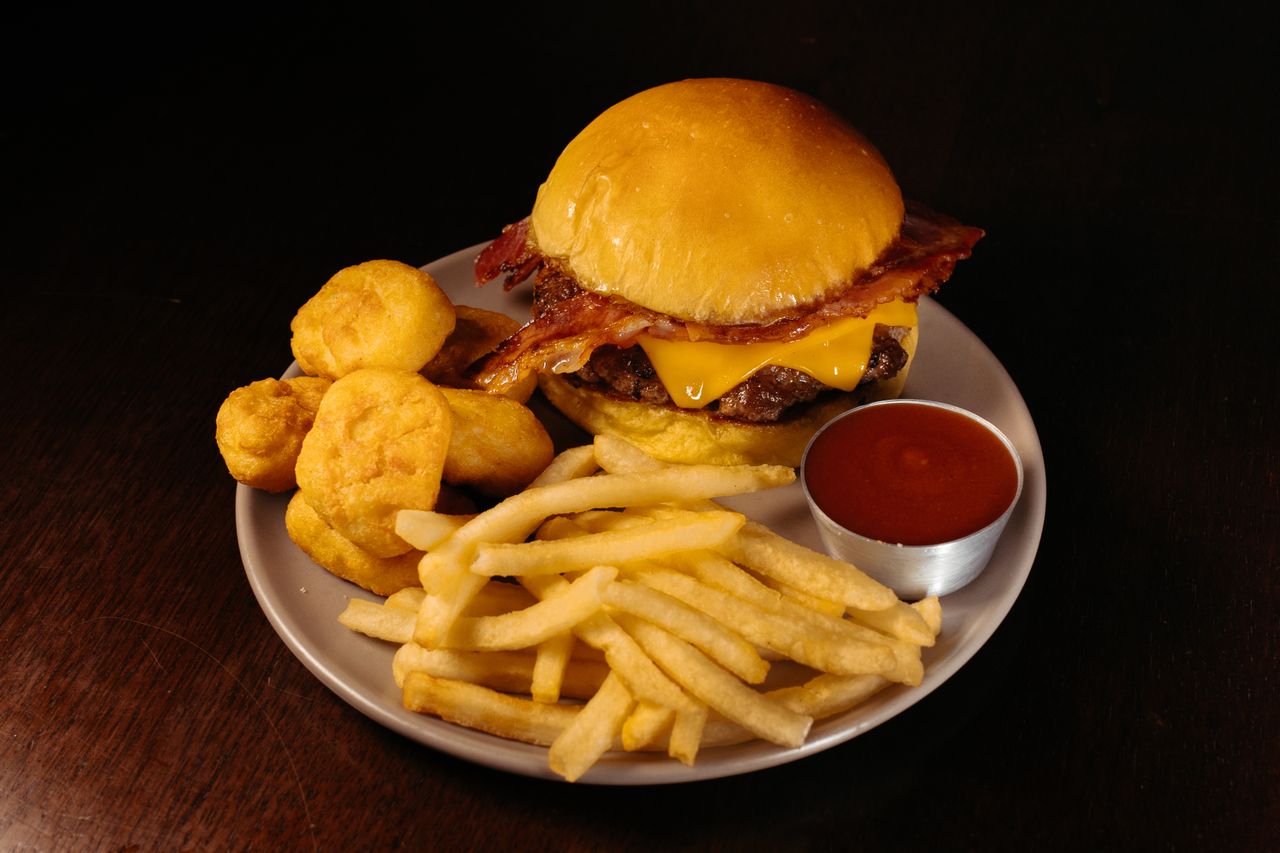 Tasty cheeseburger with bacon, fries, and nuggets on a plate with ketchup sauce.